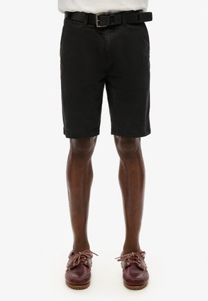 Shorts de algodón negros con corte recto, que incluyen un cinturón y una textura suave. Combinados con zapatos de barco burdeos, que exhiben detalles de cordones.