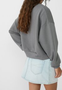 Grauer Baumwoll-Sweatshirt mit überschnittenen Schultern und geripptem Saum, kombiniert mit einem hellblauen Jeans-Minirock mit Gesäßtaschen.