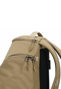 Sac à dos beige avec un haut arrondi, tissu texturé, poches à double fermeture éclair et dos noir rembourré pour le confort. Comprend une poignée supérieure.