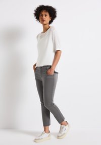 Un haut blanc texturé à manches courtes associé à un pantalon gris ajusté et des baskets légères, présentant un design simple et un style décontracté.