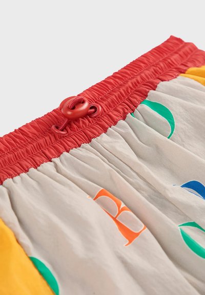 Kleurige shorts van lichtgrijs materiaal met gedurfde letters in groen, blauw en oranje; elastische rode tailleband met een bevestigingskoord.