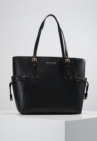 Sac fourre-tout synthétique noir avec quincaillerie dorée. Dispose de deux poignées, d'une surface texturée et d'un logo embossé à l'avant.