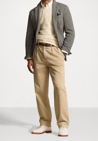 Grå herringbone-blazer, krämfärgad kabelstickad tröja, beige byxor och vita skor. Brunt läderbälte och fickfyrkant synliga.