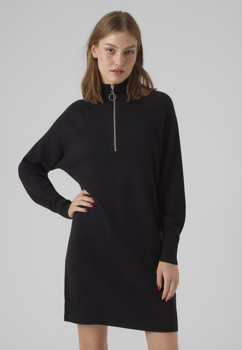 Abito nero in maglia con collo alto e dettaglio della cerniera in argento. Presenta polsini e orlo a costine, vestibilità comoda e texture morbida.