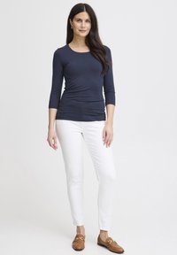 Bluză cu mâneci lungi, culoare bleumarin, cu gât rotund, pantaloni albi mulați și mocasini maro. Material fin, croială slim și lungime până la mijlocul șoldului.