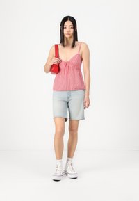 Raudonas ir baltas langelių rašto tank top su reguliuojamomis petnešėlėmis ir rišamu priekyje, derinamas su šviesiai mėlynomis džinsinėmis šortais ir baltais sportbačiais.