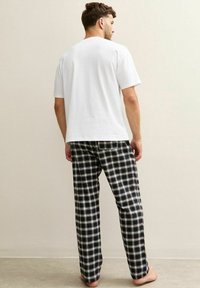 Vêtements de nuit pour hommes comprenant un t-shirt blanc uni à manches courtes et un pantalon de pyjama à carreaux noirs avec des lignes blanches et grises, en tissu de coton, coupe décontractée.