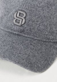 Siva vunena baseball kapica s reljefnim izvezenim međusobno povezanim "SB" logom na prednjem panelu, vidljiva tekstura tkanine.
