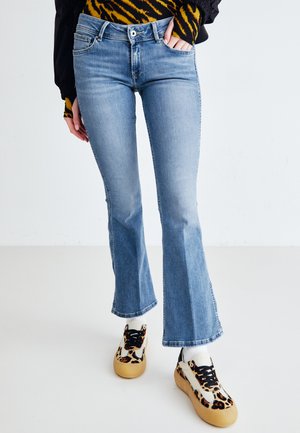 Jean flare bleu clair avec un délavage moyen, présentant une fermeture à bouton et zip, des poches frontales et un ourlet propre. Associé à des baskets à motifs.