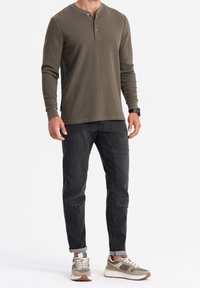 Dlouhý olivově zelený henley s knoflíkovým rozparkem, v kombinaci s černými zúženými džíny a světle šedými a béžovými teniskami.