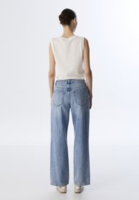 Top bianco senza maniche abbinato a jeans a gamba larga di colore azzurro chiaro. I jeans presentano tasche posteriori e una vestibilità rilassata, con un orlo grezzo.