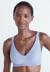 Lys blå sømløs bralette med dyp V-hals, brede stropper og glatt tekstur. Har en støttende passform og minimalistisk design.