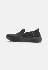 Svarta slip-on skor med ett andningsbart mesh-övre och texturerade accenter. Har en flexibel sula och minimalistisk design.