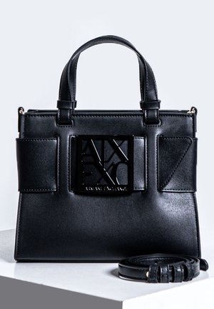 Petit sac à main en cuir noir avec un design structuré, mettant en avant un logo distinctif sur le devant, des poignées doubles et une bandoulière amovible.