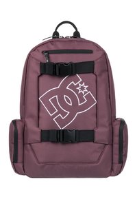 Mochila marrón con correas y hebillas negras. Presenta un gran logo blanco en la parte frontal. Hecha de un tejido duradero con bolsillos laterales con cremallera.