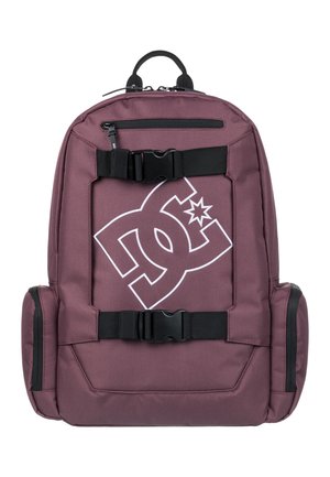 Mochila marrón con correas y hebillas negras. Presenta un gran logo blanco en la parte frontal. Hecha de un tejido duradero con bolsillos laterales con cremallera.