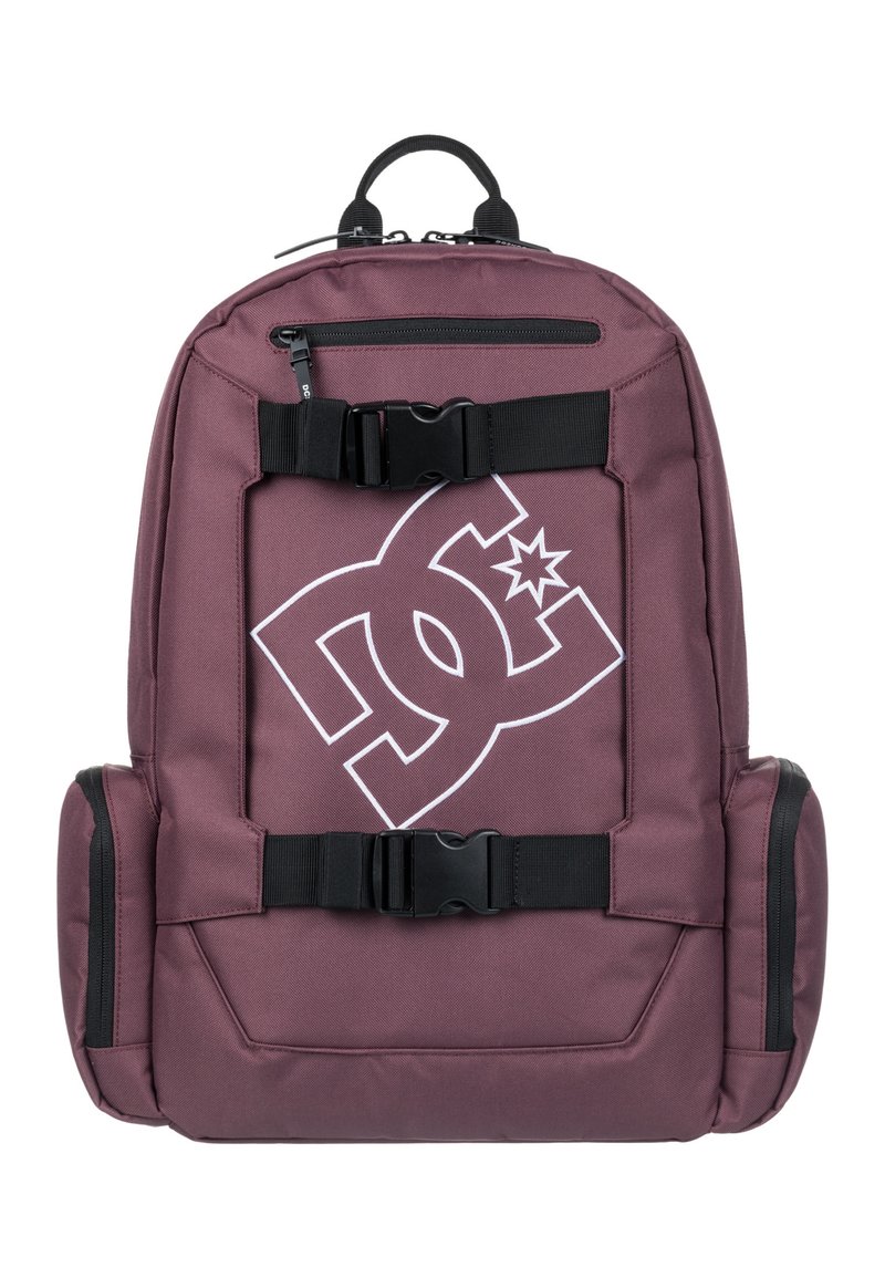 Mochila marrón con correas y hebillas negras. Presenta un gran logo blanco en la parte frontal. Hecha de un tejido duradero con bolsillos laterales con cremallera.