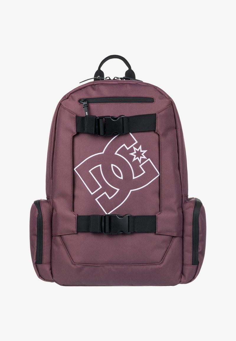 Mochila marrón con correas y hebillas negras. Presenta un gran logo blanco en la parte frontal. Hecha de un tejido duradero con bolsillos laterales con cremallera.