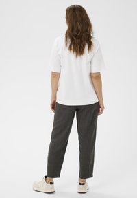Wit kortmouwtop, gecombineerd met donkergrijze tapered broek. Schoenen zijn lichtbeige met zwarte accenten. Soepele textuur, casual pasvorm.