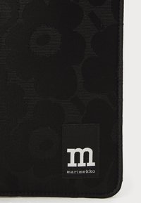 Sort stof tabletetui med et struktureret blomstermønster, med en syet sort etiket der viser mærket "marimekko" og et hvidt logo.