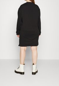 Černé oversized mikinové šaty s dlouhými rukávy, žebrovanými manžetami a rovnými lemy, v kombinaci s bílými šněrovacími kotníkovými botami.