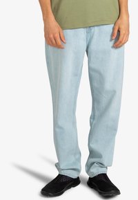 Jean bleu clair en denim, présentant une coupe décontractée et un design simple, associé à des baskets noires texturées.