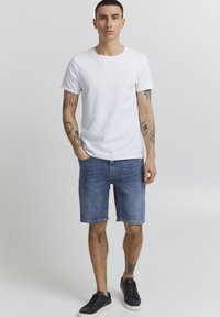 Camiseta de algodón blanca, pantalones cortos de denim azul y zapatillas negras. Los pantalones cortos son de longitud a la rodilla con un ligero desgaste, y las zapatillas tienen un diseño elegante.