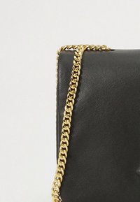 Black leather handbag with a gold chain strap draped over the corner against a plain light background.