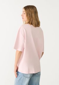 Lichtroze oversized katoenen t-shirt met korte mouwen, ronde halslijn en een gladde textuur; gedragen met lichtblauwe denim jeans.