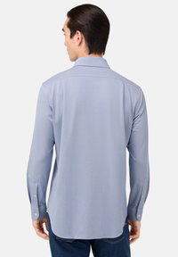 Camicia azzurra a maniche lunghe con colletto button-down, tessuto testurizzato e polsini con bottone. Presenta un orlo arcuato e dettagli sul retro.