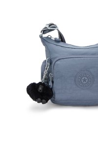 Borsa a tracolla blu in nylon con tasca frontale, superficie texture e portachiavi a forma di gorilla nero. Logo circolare Kipling impresso sul lato.
