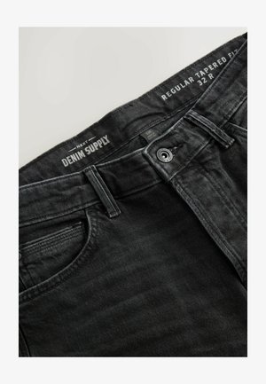 Jean en denim noir avec une coupe fuselée. Les caractéristiques incluent une fermeture à bouton, des poches avant et des détails de couture sur le tissu.