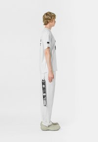 Camiseta blanca de manga corta con estampado gráfico negro, combinada con pantalones blancos que tienen detalles de etiqueta negra y calzado oversize texturizado.