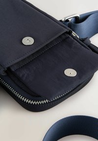 Borsa in tessuto blu navy con chiusura a zip, dettagli in fibbia argentata e manico intrecciato. La borsa presenta una superficie liscia e un design pratico.