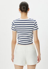 Marinblå och vit randig crop top med korta ärmar, ribbad textur, i kombination med vita shorts med bakfickor och en slät yta.