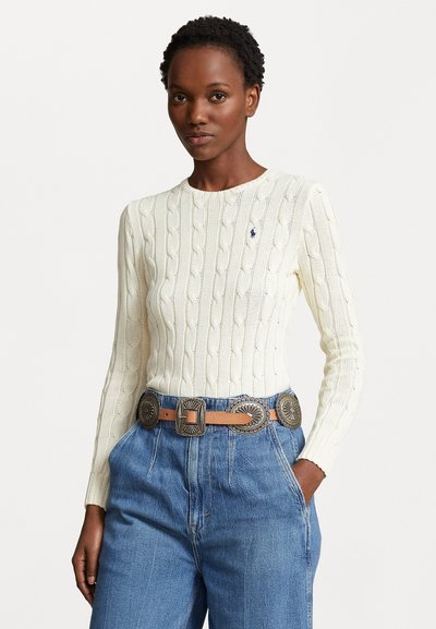 Crème-coloured kabelgebreide trui met ronde hals en lange mouwen, gecombineerd met hoge taille blauwe denim jeans en een bruin leren riem met zilveren accenten.
