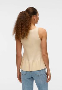 Hellbeige, gerippter Tanktop mit schwingendem Peplum-Saum, kombiniert mit hellblauen Jeans. Glatte Textur, ärmelloses Design, minimalistischer Stil.