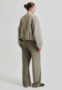 Grå oversized genser med elastisk kant, sammen med høy-vidde olivengrønne bukser. Svarte sko med nettingdetaljer.