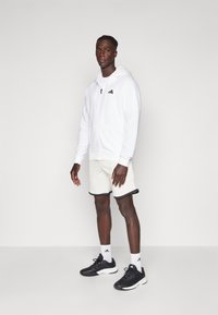 White zip-up hoodie with black accents, paired with light-colored shorts featuring dark trim and black athletic shoes. Simple and functional design.