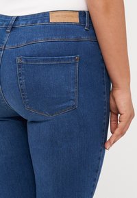 Jeans in jeans scuro attillati, con una tasca posteriore, etichetta marrone in vita e dettagli di cucitura a contrasto.