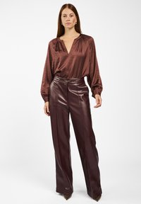 Donkerbruin satijnen blouse met een V-hals en geplooide details, gecombineerd met hoge burgundy neplederen broeken en puntige hakken.