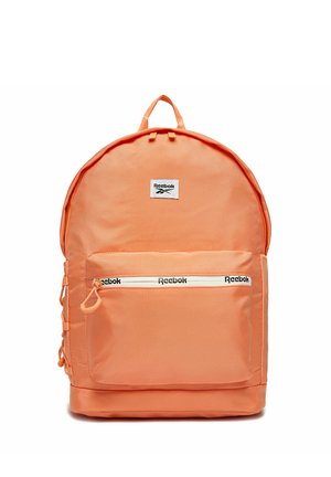 Jasno pomarańczowy plecak Reebok z przednią kieszenią na zamek błyskawiczny, na której jest logo Reebok na zamku i naszywka nad kieszenią.