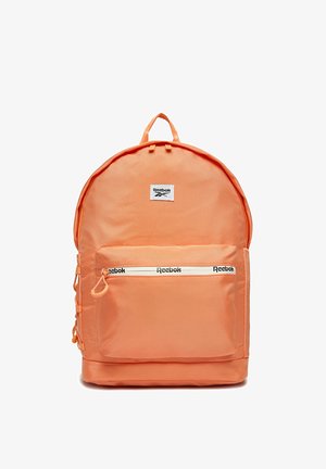 Jasno pomarańczowy plecak Reebok z przednią kieszenią na zamek błyskawiczny, na której jest logo Reebok na zamku i naszywka nad kieszenią.