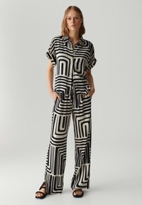 Schwarzes und weißes gemustertes Outfit bestehend aus einem kurzärmeligen, knöpfbaren Hemd und weit geschnittenen Hosen, gefertigt aus einem glatten, leichten Material.