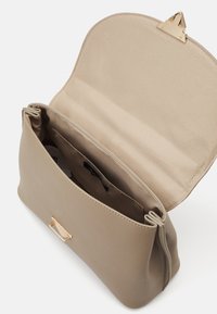 Beige handväska i slät material, med ett guldspänne, två fack och ett mjukt foder. Dragkedja för enkel åtkomst.