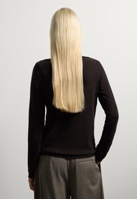 Maglione a maniche lunghe marrone in maglia, con texture semplice e collo a girocollo, abbinato a pantaloni grigi a gamba larga. Vista posteriore, capelli lunghi e biondi lisci visibili.