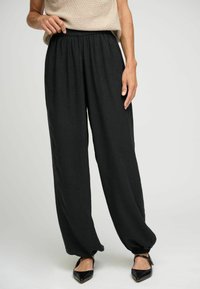 Pantaloni neri a gamba larga con vita elasticizzata. Tessuto leggero con una texture liscia. Caviglie orlate e abbinati a ballerine nere a punta.