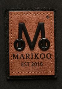 Hnědá kožená nášivka s vyraženým černým textem "MARIKOO" a "EST 2016", s stylizovaným písmenem "M" začleněným do designu.