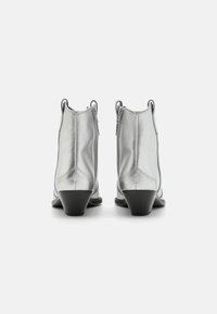 Botines plateados con un acabado metálico elegante, que presentan puntera cerrada, cierre con cremallera y un tacón negro ligeramente elevado.