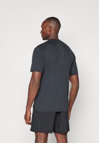 T-shirt de sport noir à manches courtes, avec trois rayures verticales au dos, associé à un short foncé, texture de tissu lisse.